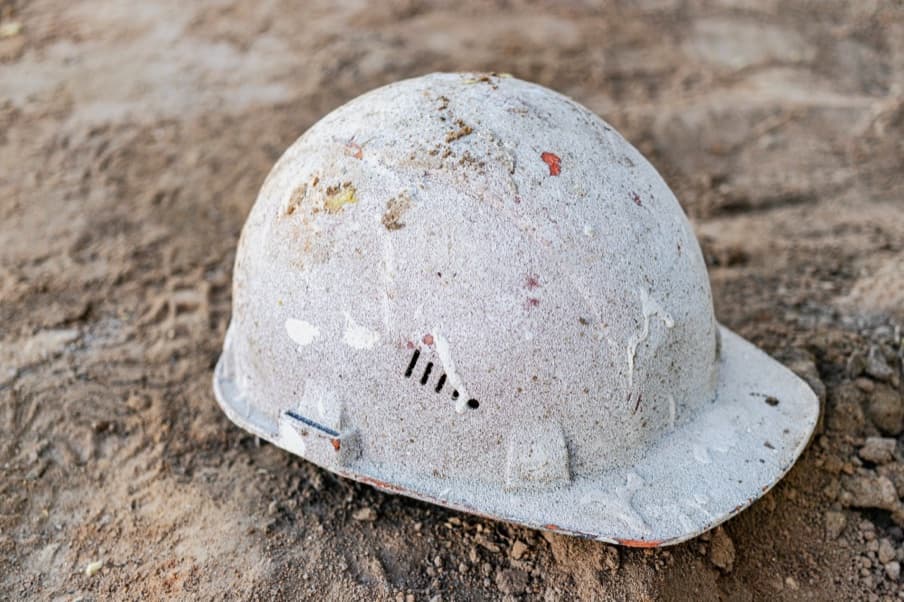 A damaged hard hat abandoned on bare ground